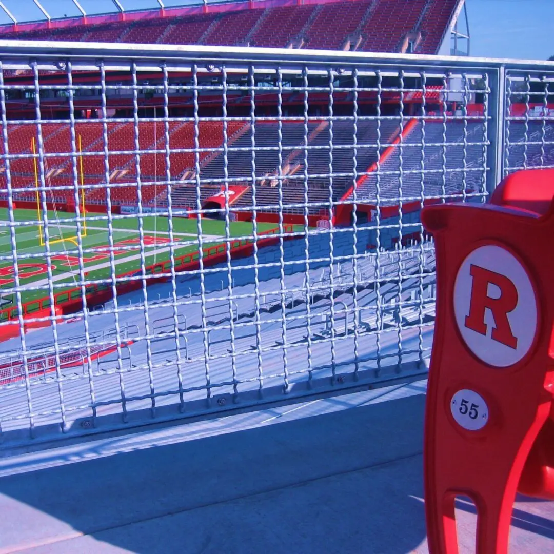 A red chair in front of a fence with a stadium behind it.