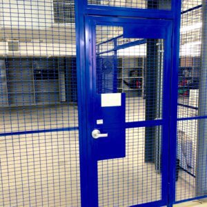A blue door in an industrial building with a metal fence.