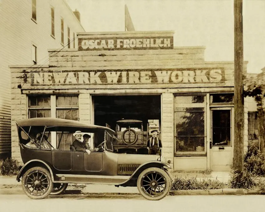 An old photo of a car parked in front of a wire works.