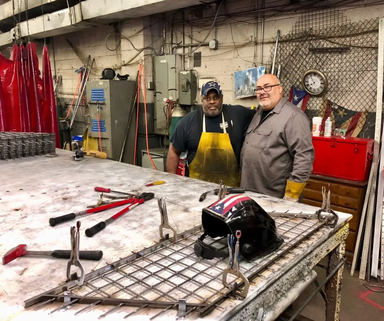 Two men standing in a room with tools on the table.